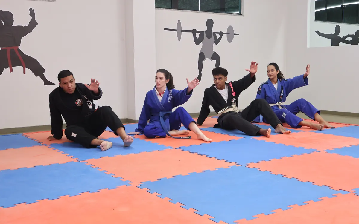 Alunos de quimono treinam jiu-jitsu no tatame do colégio
